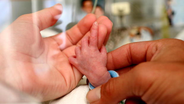 Parents hold the hand of a premature baby in hospital