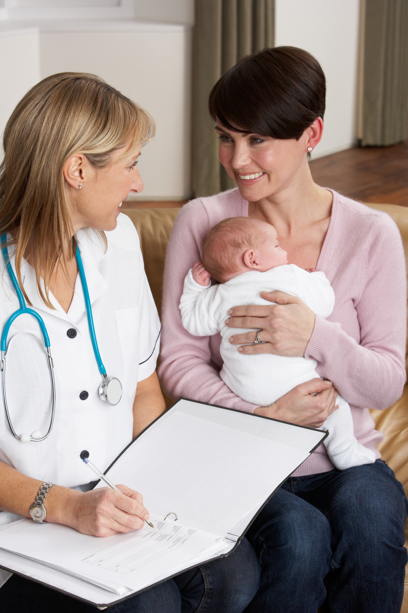 A smiling mother holds her newborn whilst listening to a doctor